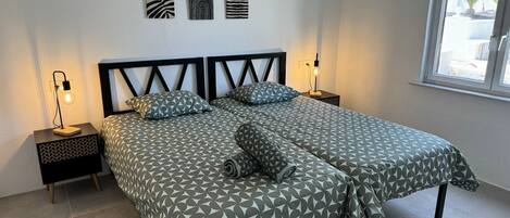 Una cama doble con ropa de cama de diseño geométrico, dos mesitas de noche con lámparas y tres obras de arte en la pared sobre la cama.