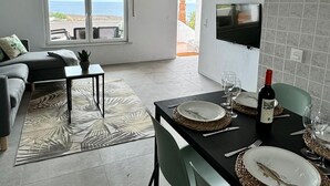 A modern living room with a sofa, a coffee table, and a dining area with a table set for two. - Ferienwohnung in Einer Finca 4000m2 mit Pool Naehe Puerto Calero (Mácher)