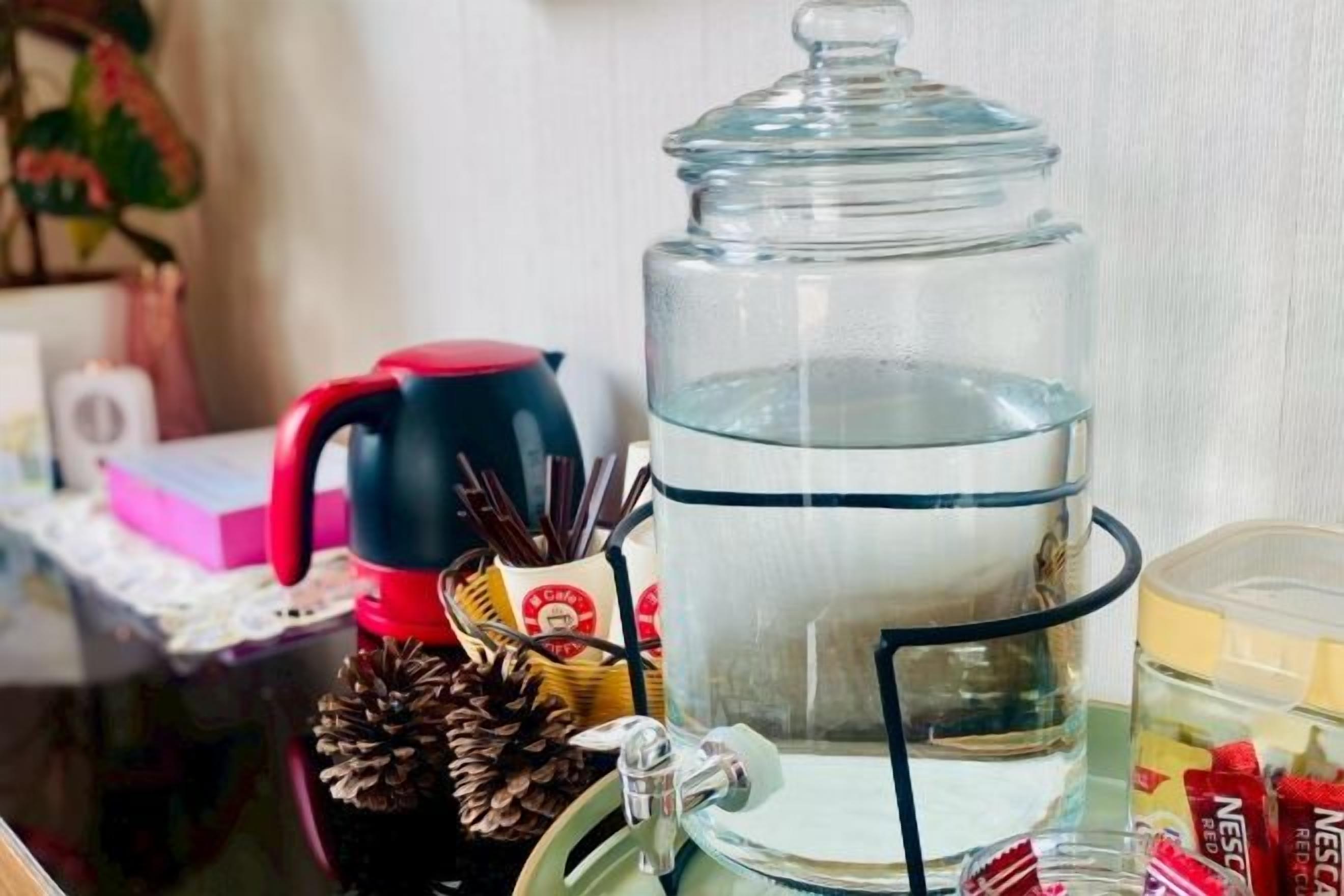 Un dispensador de agua de vidrio con tapa, una tetera roja, una cafetera y un recipiente con tapa.