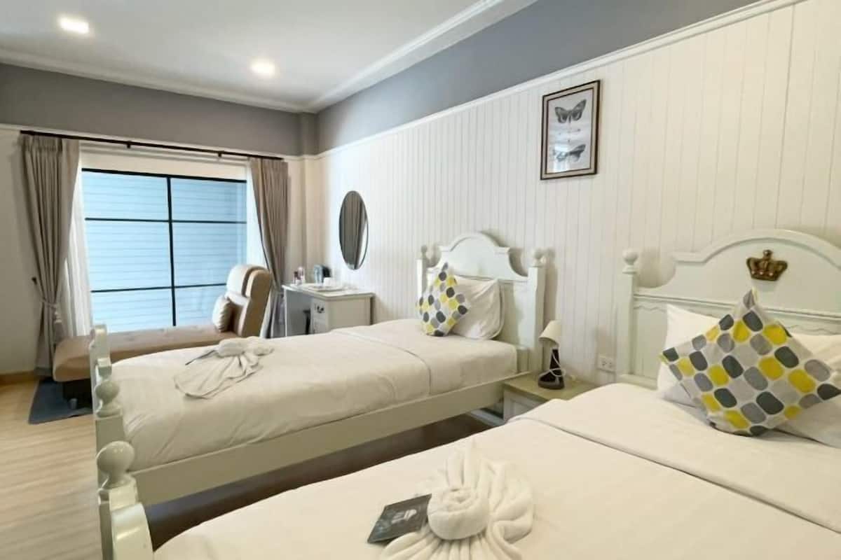Une chambre d’hôtel avec deux lits, une table de chevet, un miroir, une fenêtre avec des rideaux et un tableau encadré au mur.