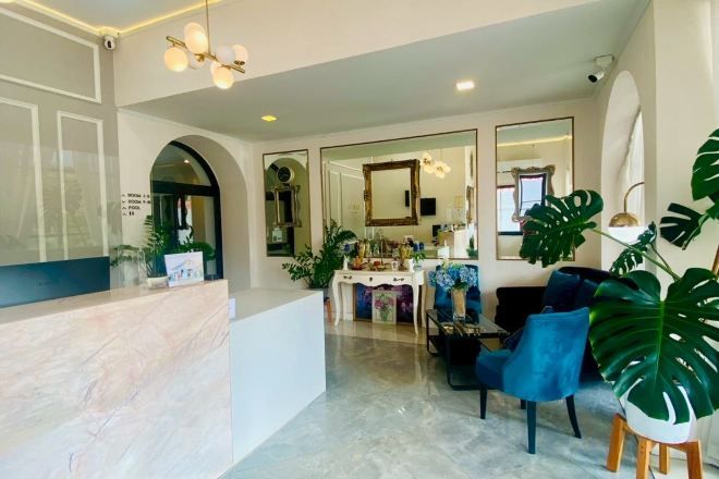 A reception area with a marble counter, a seating area with blue chairs, and large green plants.