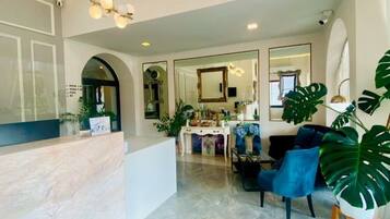 A reception area with a marble counter, a seating area with blue chairs, and large green plants.