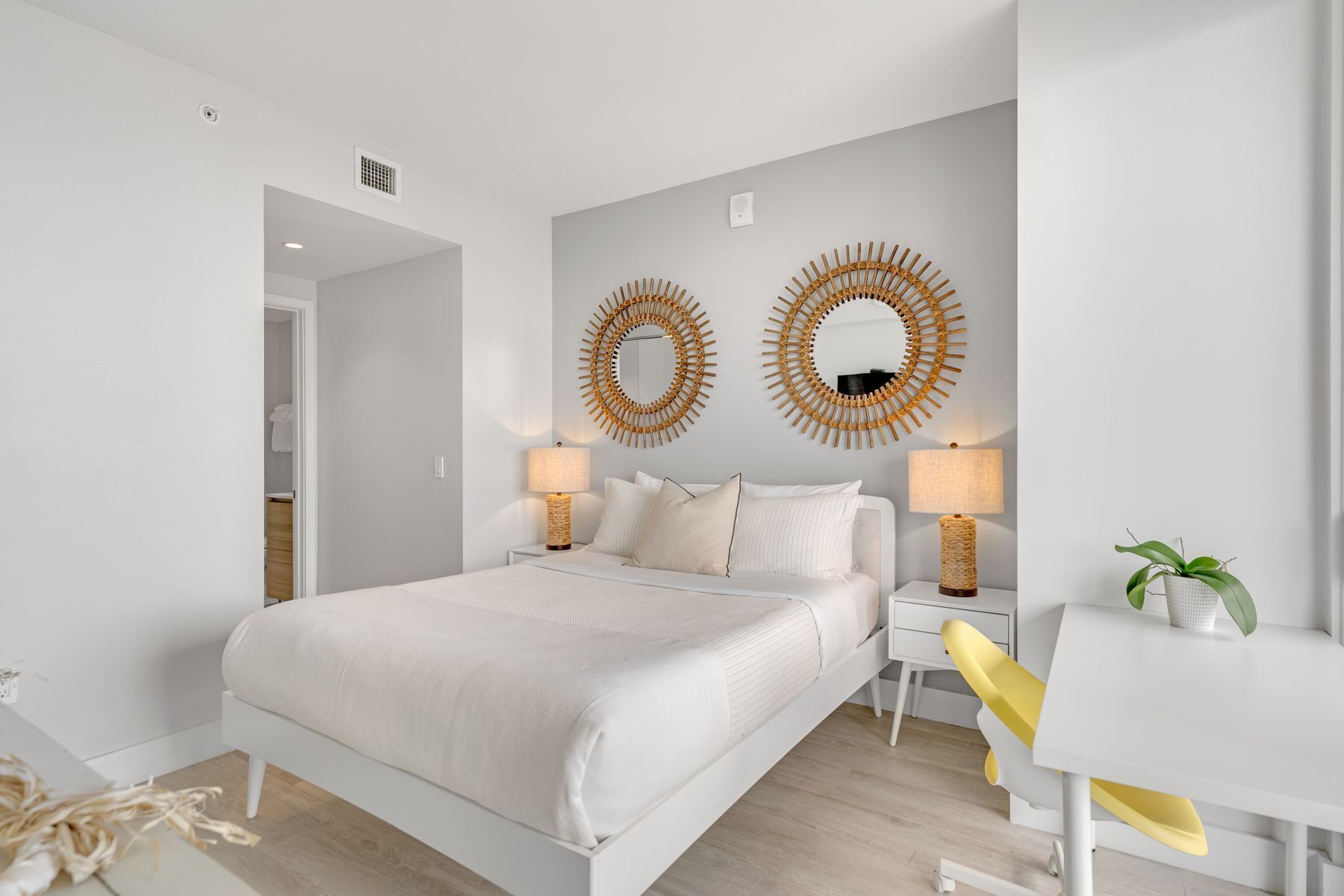 A modern bedroom with a large bed, two bedside lamps, and two wall-mounted mirrors.