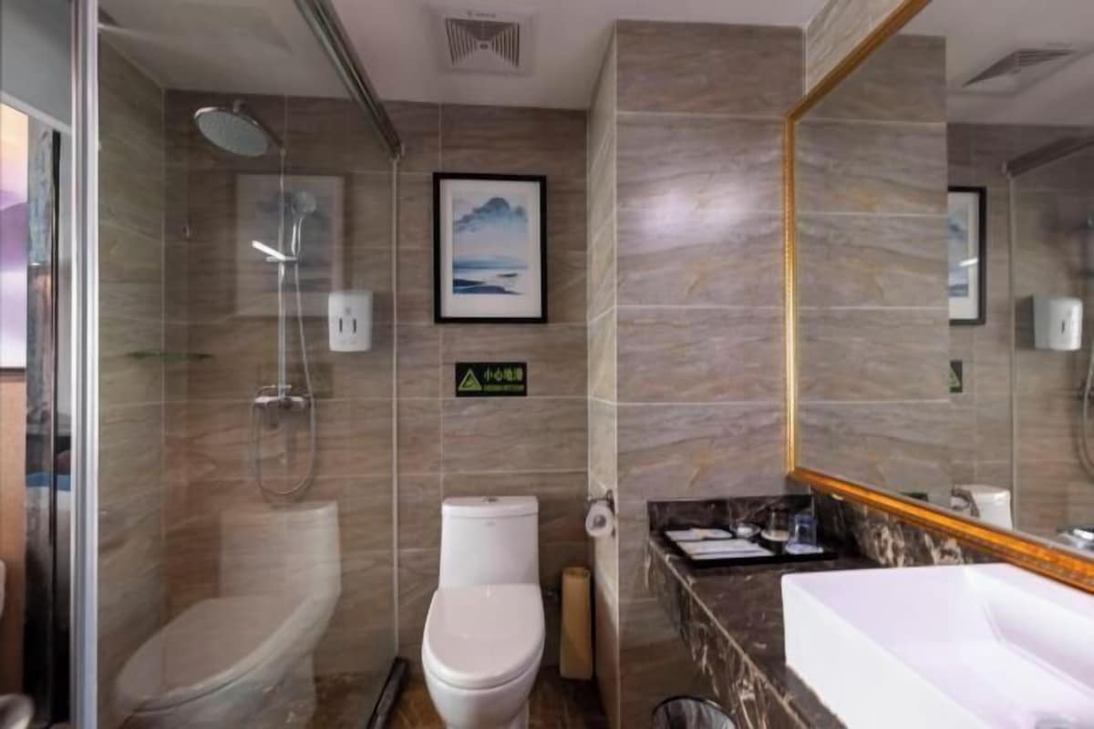Ein Badezimmer mit Dusche, Toilette und Waschbecken, Marmorwänden und einem gerahmten Bild an der Wand.