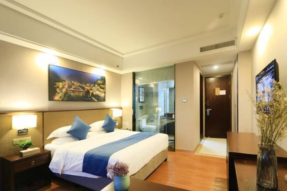 A hotel room with a bed, bedside tables, a TV, and a painting on the wall.