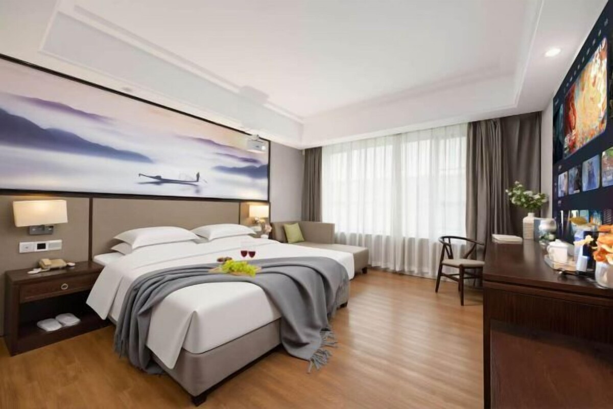 A hotel room with a large bed, bedside tables, a desk, and a large window with curtains.