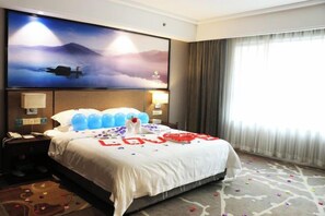 Una camera d'albergo con un letto grande, una televisione a schermo piatto appesa al muro e una finestra con tende.