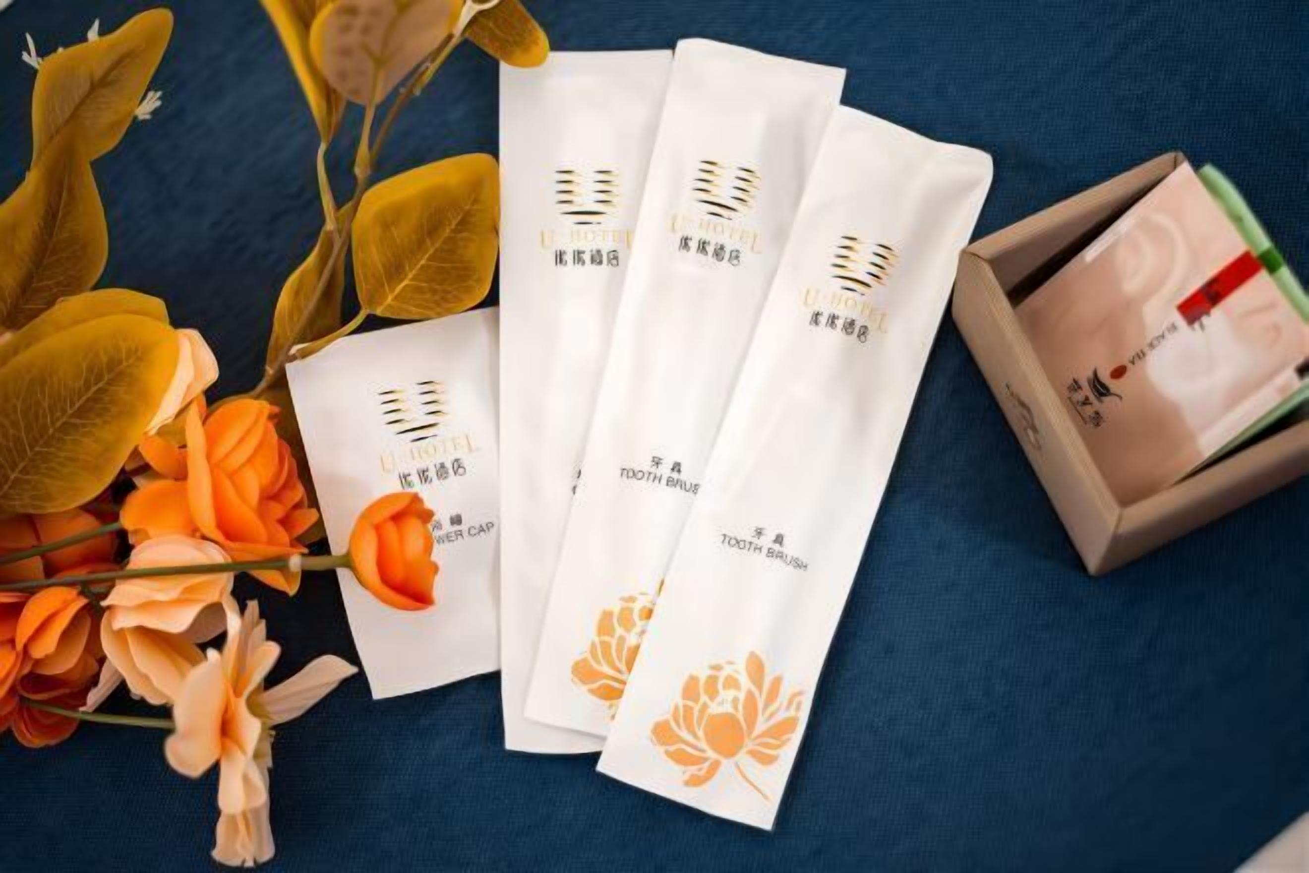 Four packages of a product with a floral design, placed on a blue surface with some flowers and a box nearby.