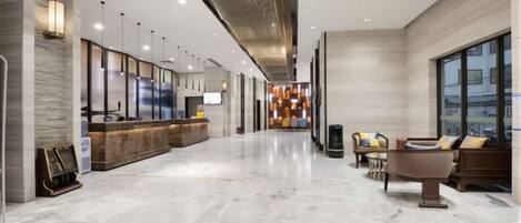 A hotel lobby with a reception desk, seating area, and a modern chandelier.