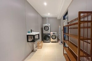 A laundry room with a washing machine, dryer, and shelves with folded clothes. - Yoyo Hotel (Zhongshan Bus Terminal) (Zhongshan)