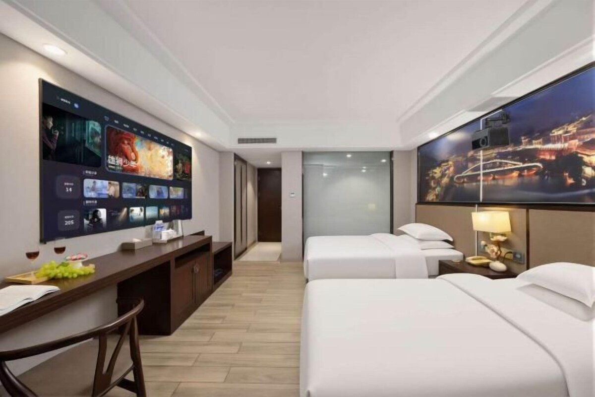 A hotel room with a flat-screen TV, a desk, two beds, and a cityscape view.