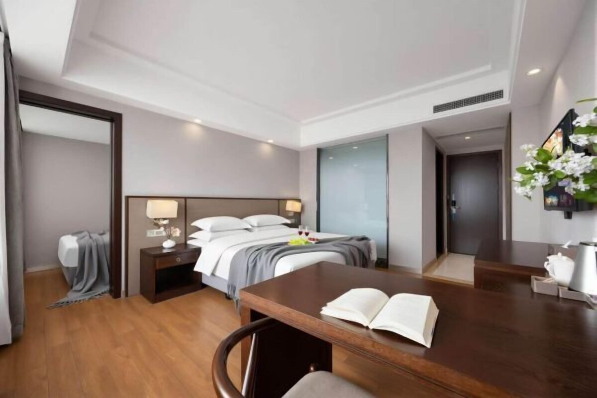 A hotel room with a bed, bedside tables, a desk with an open book, and a chair.