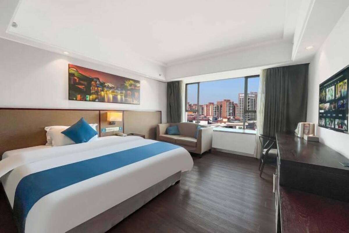 A hotel room with a large bed, a desk, a chair, a TV, and a painting on the wall.