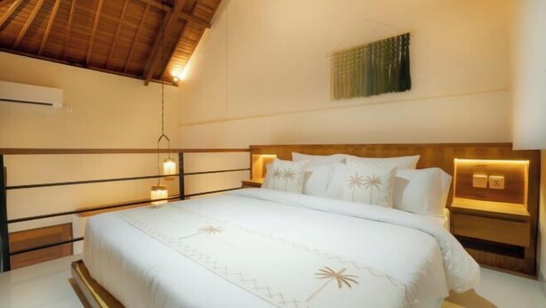 A bedroom with a bed, bedside lamps, a wall-mounted air conditioner, and a ceiling fan. - Sleepwell Seminyak (Bali)