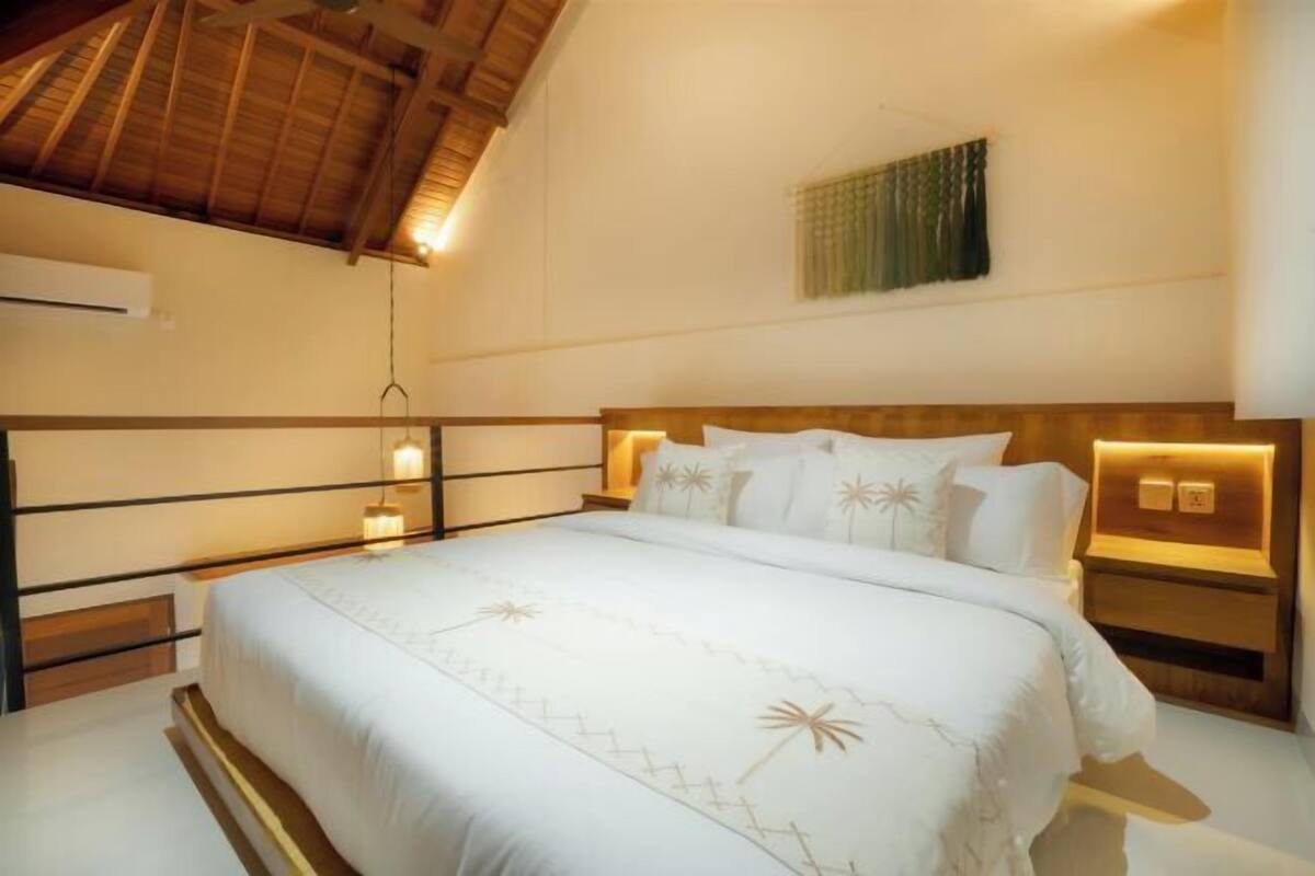 Un dormitorio con una cama, lámparas de noche, aire acondicionado en la pared y un ventilador de techo.
