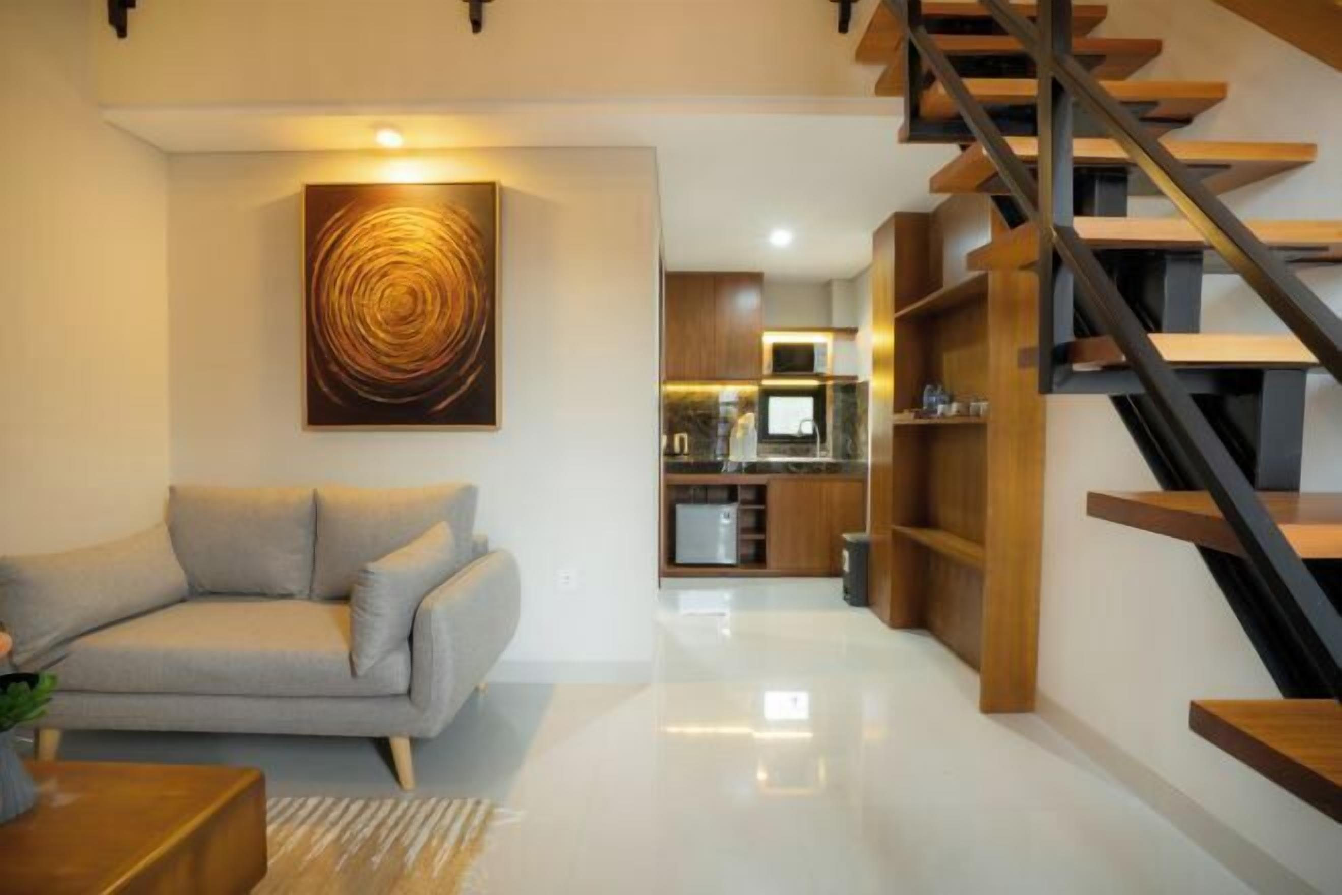 A modern living room with a sofa, a coffee table, a painting, and a staircase leading to a kitchen area.