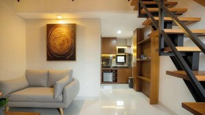 A modern living room with a sofa, a coffee table, a painting, and a staircase leading to a kitchen area. - Sleepwell Seminyak (Bali)