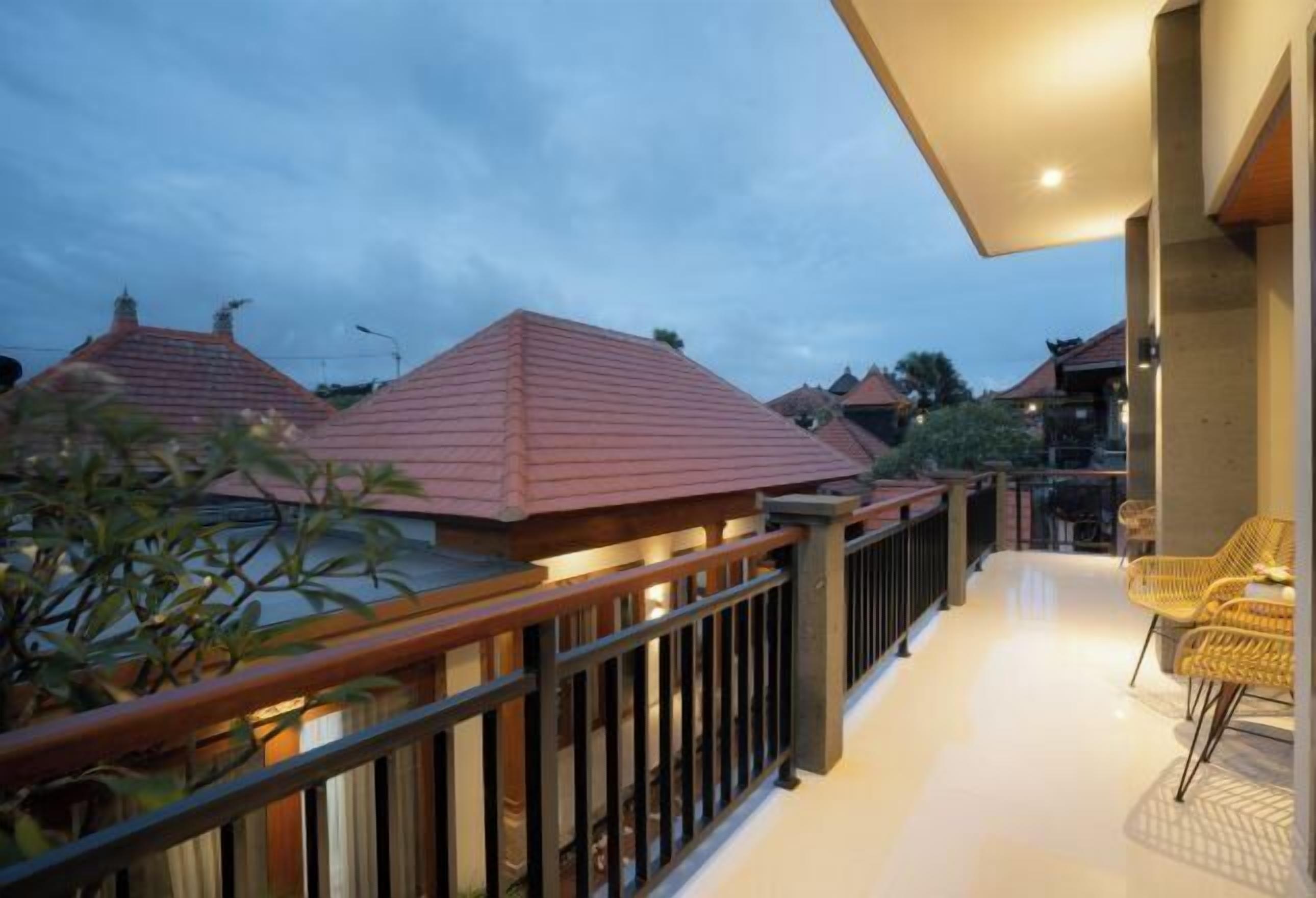 A balcony with a railing, a potted plant, and a seating area with chairs.