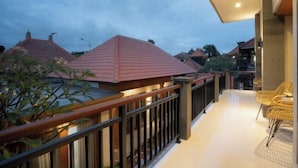 A balcony with a railing, a potted plant, and a seating area with chairs. - Sleepwell Seminyak (Bali)