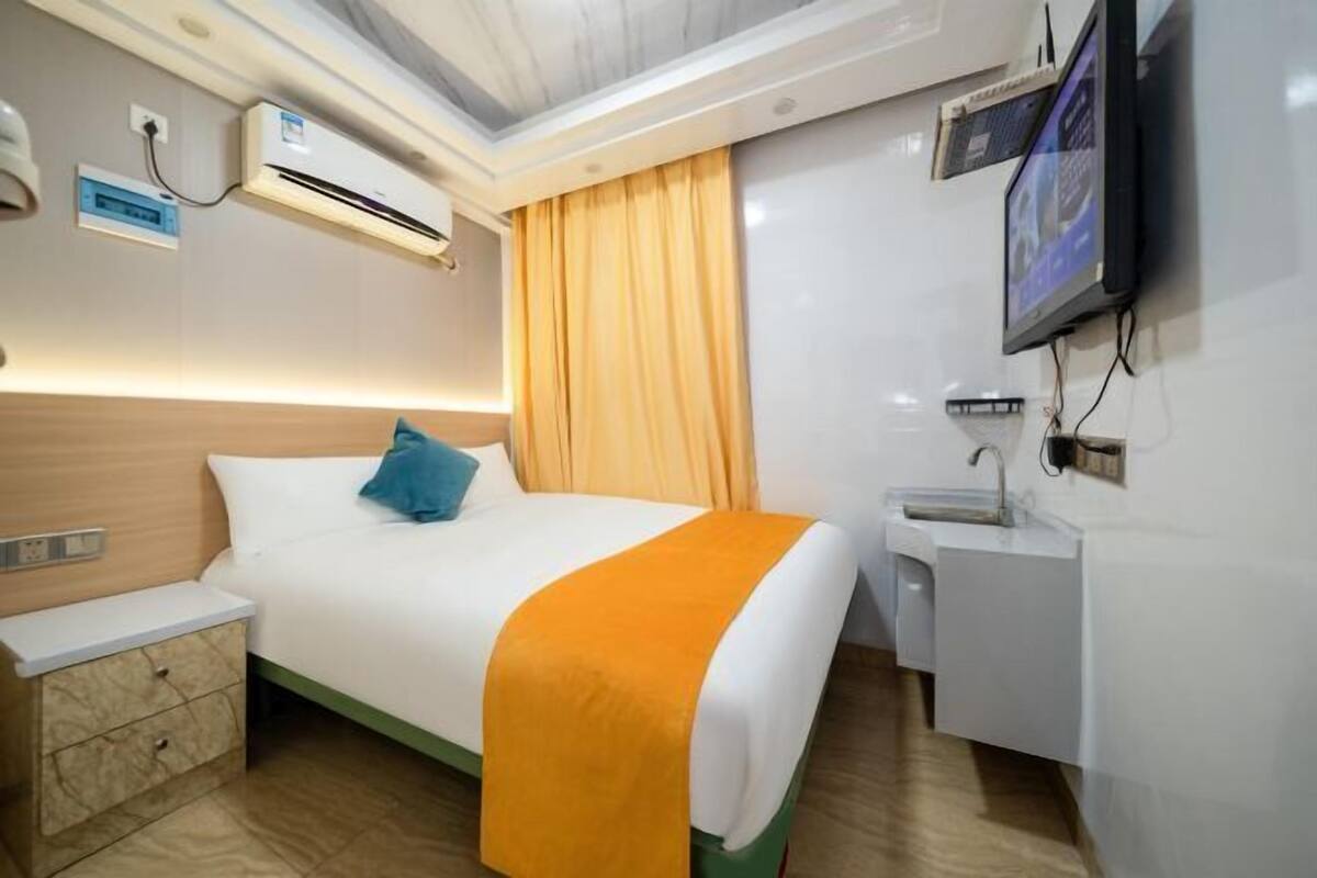 A hotel room with a bed, a nightstand, a desk with a sink, an air conditioning unit, and a television.