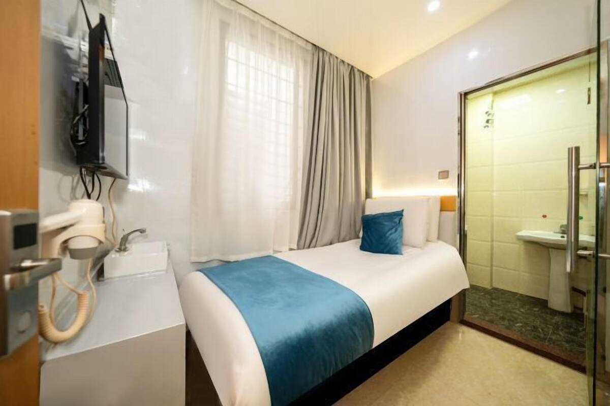 A hotel room with a bed, a bedside table with a phone, a lamp, and a bathroom with a sink and mirror.