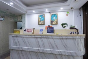 A marble reception desk with a number plate, two framed artworks, and a potted plant. - Zhangzhou Guanghua Hotel (Zhangzhou)