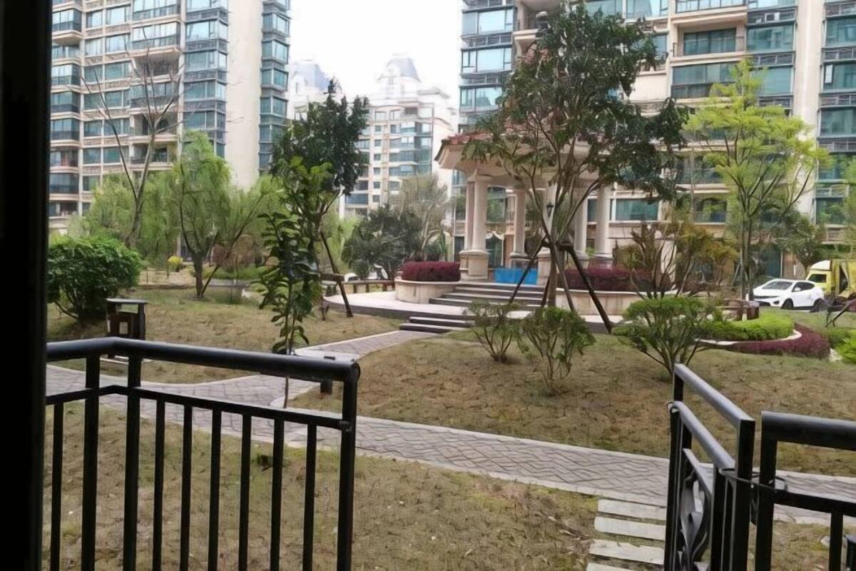 A residential area with a paved walkway, small trees, and a white car parked in the distance.