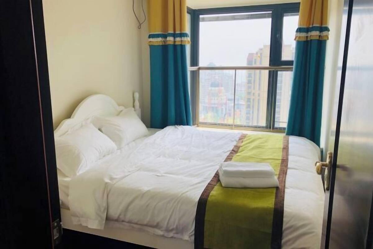 A hotel room with a bed, curtains, and a window with a view of buildings.