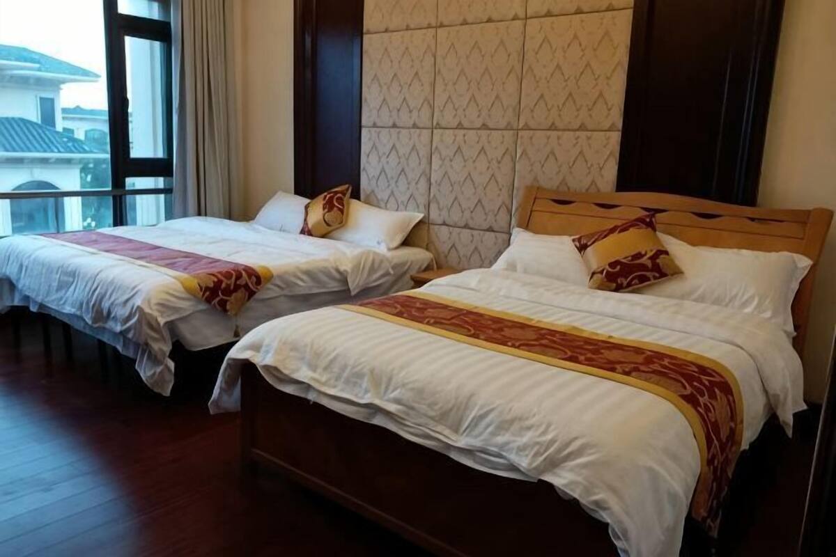 Two double beds with wooden frames, a patterned wall, and a window with curtains.