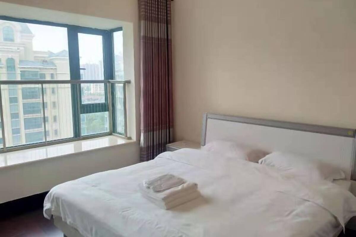A hotel room with a large window, a bed, and a view of buildings.