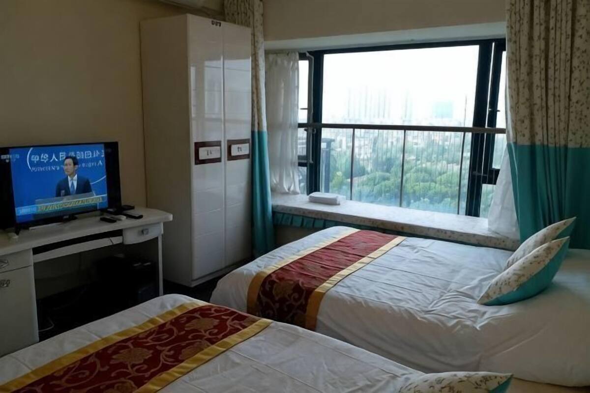A hotel room with two beds, a TV, a wardrobe, and a window with a view.
