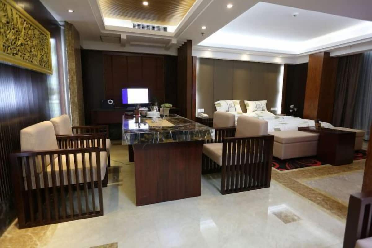 Une chambre d’hôtel moderne avec un îlot en marbre, un ensemble de canapés, un lit et un téléviseur en arrière-plan.