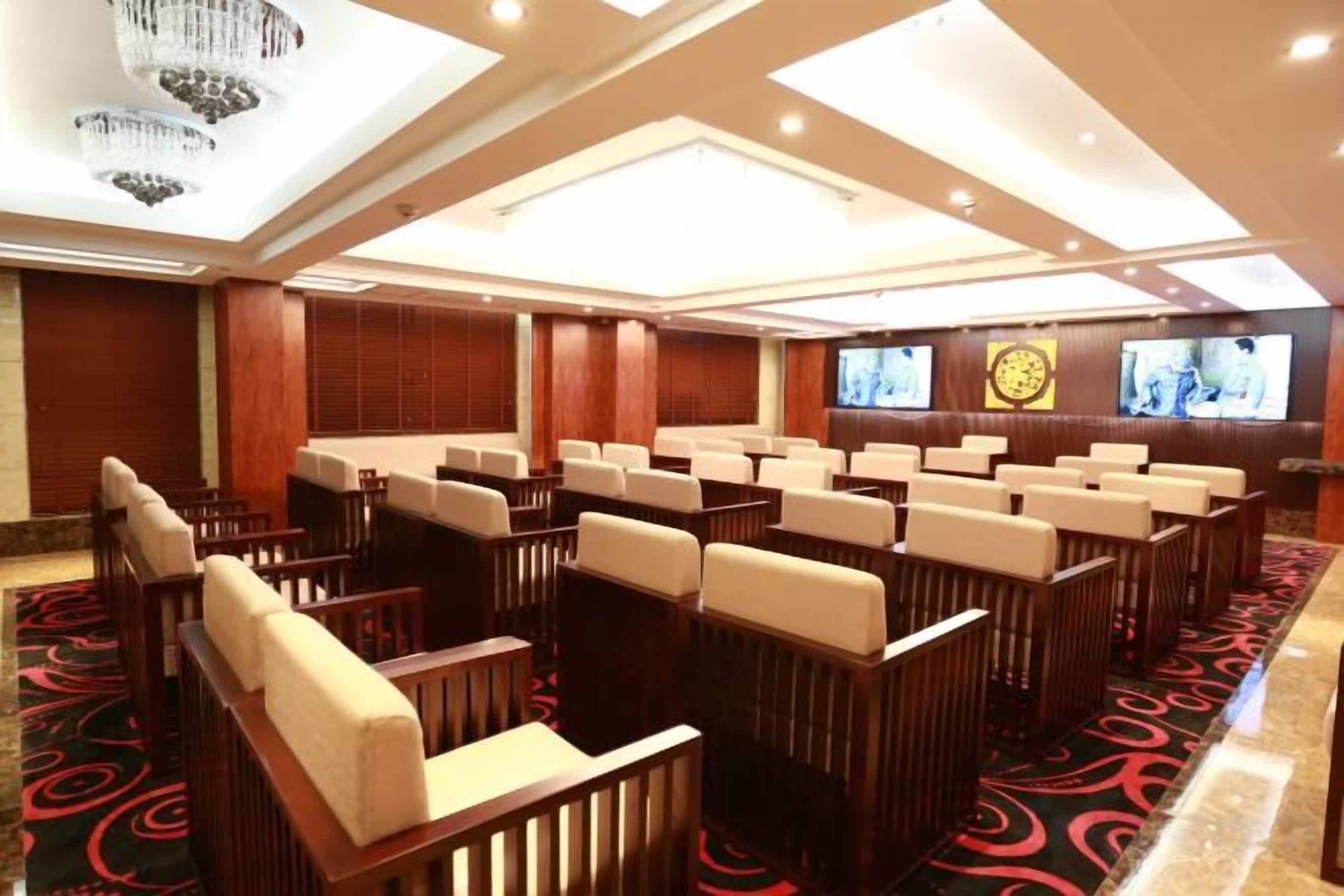 A conference room with rows of chairs, a large screen, and a carpeted floor.