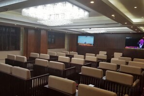 A conference room with rows of chairs, a large screen, and a chandelier.