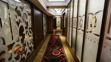 A hotel corridor with a patterned carpet, decorative panels, and a reception area in the distance.