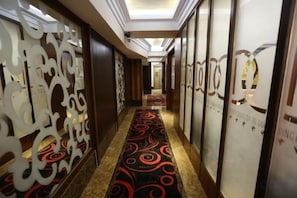 Un pasillo de hotel con alfombra estampada, paneles decorativos y una recepción a lo lejos.