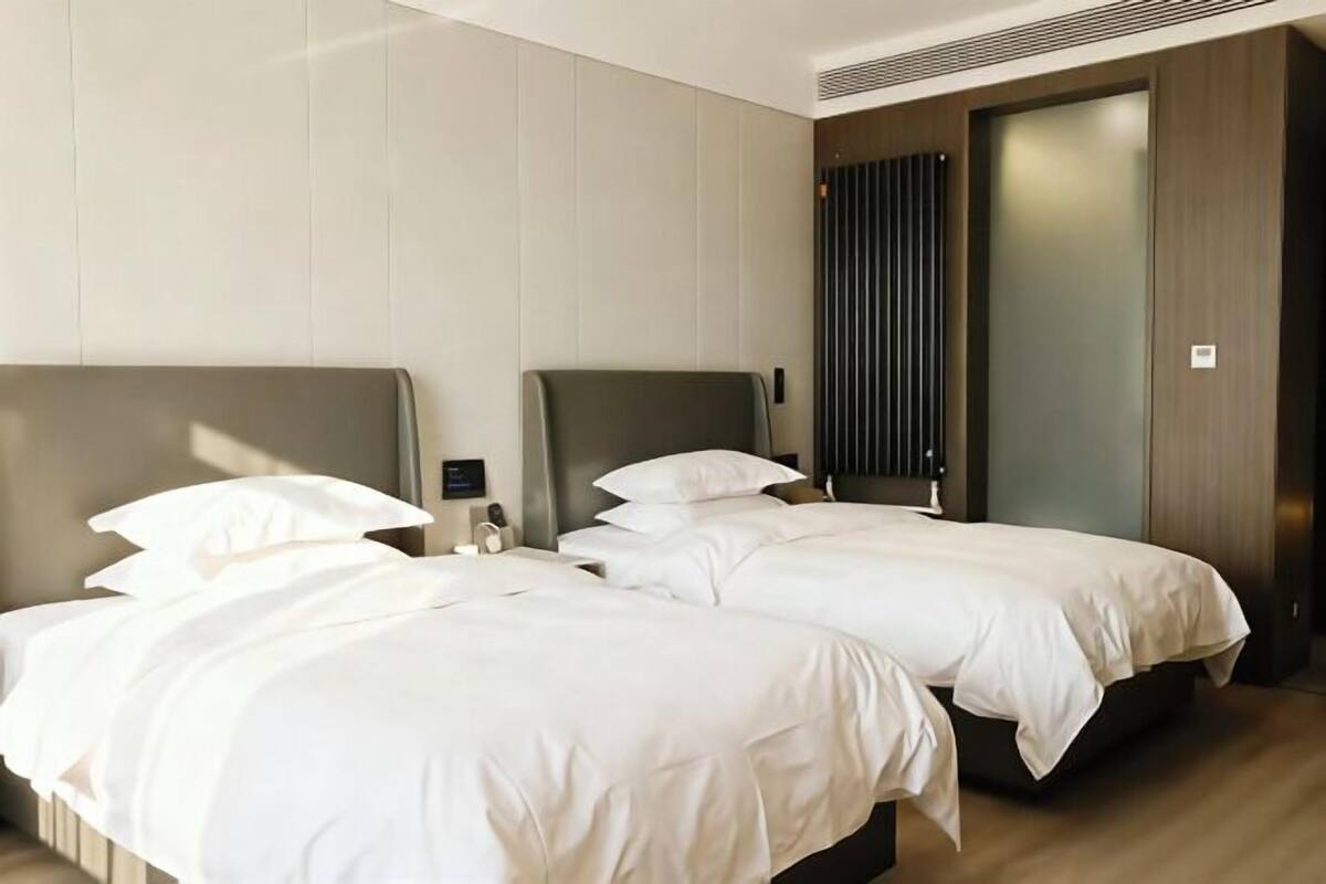 A hotel room with two beds, a nightstand, and a door with a vertical blinds design.