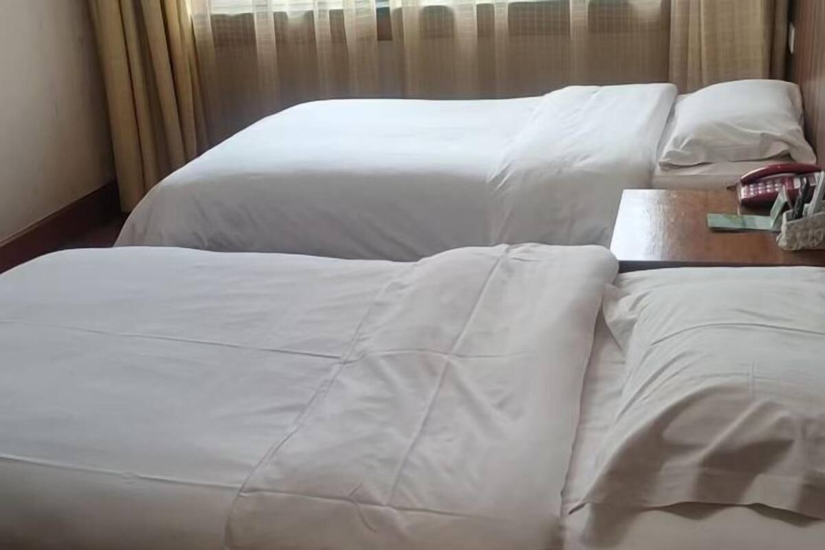 A hotel room with two beds, a wooden nightstand, and a window with curtains.