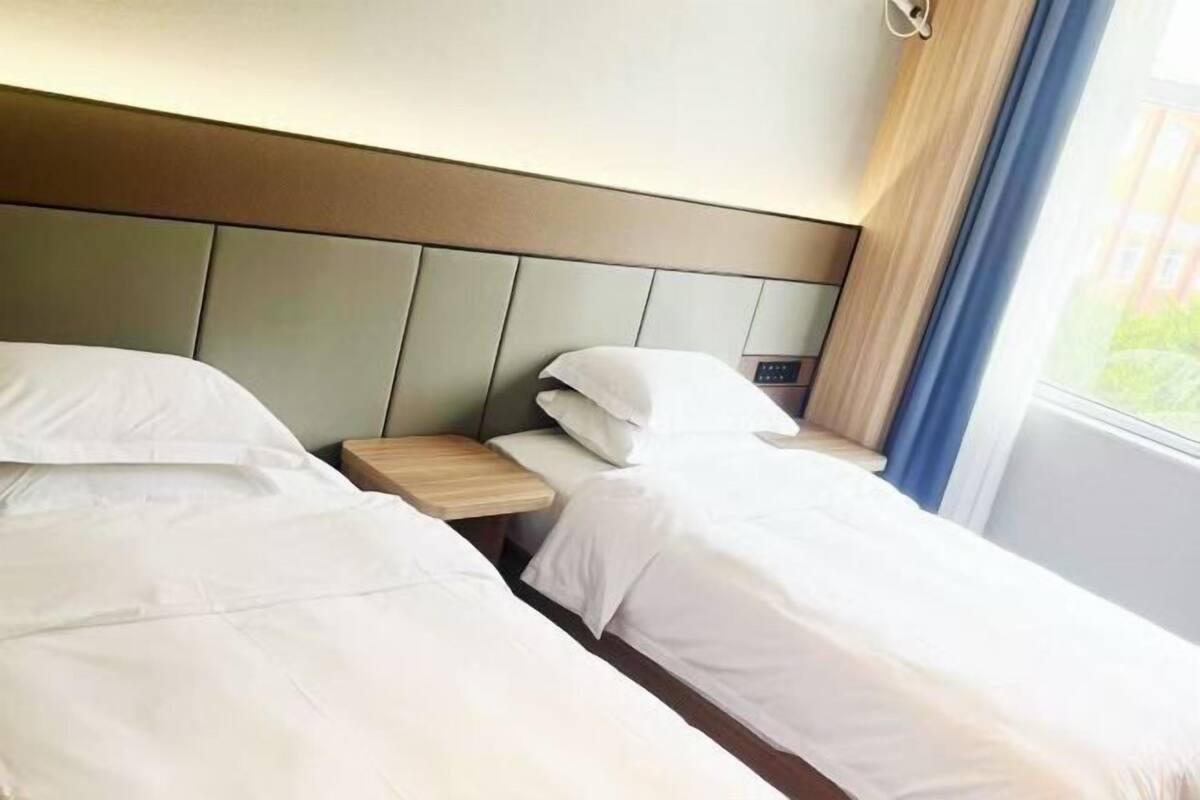 A hotel room with two single beds, a bedside table with a lamp, and a window with curtains.
