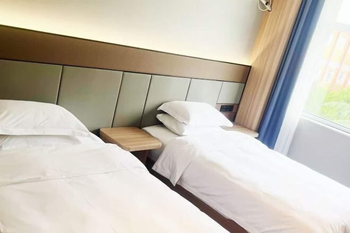 A hotel room with two single beds, a bedside table with a lamp, and a window with curtains.