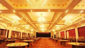 Un gran salón de baile de hotel, ornamentado, con candelabros, mesas redondas y alfombra roja.