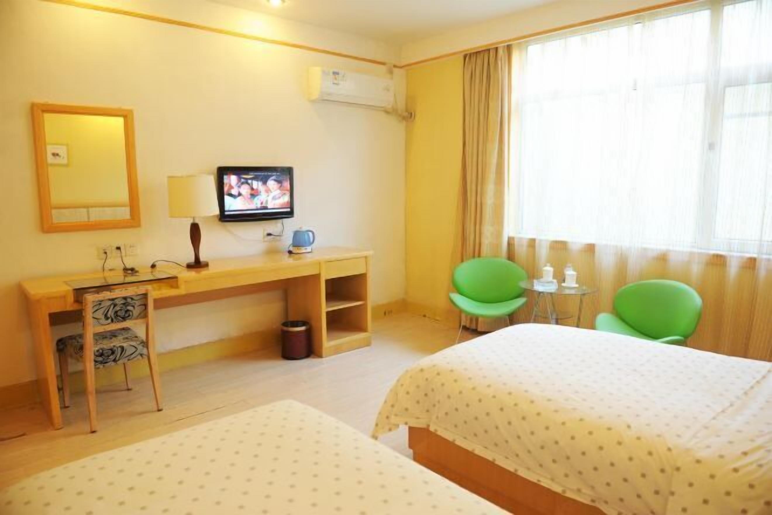 A hotel room with two beds, a desk with a television, a small table, and two green chairs.