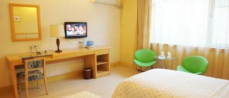 A hotel room with two beds, a desk with a television, a small table, and two green chairs.