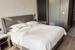 A modern hotel room with a large bed, a bedside table, and a built-in heater. - Rushan Hotel (Rushan)