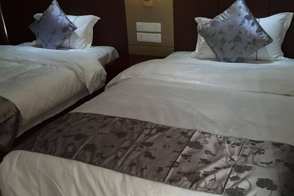 A hotel room with two beds, each with white bedding and floral-patterned pillows.
