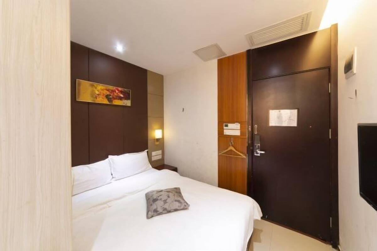 A hotel room with a bed, a wardrobe, a wall-mounted TV, and a painting.