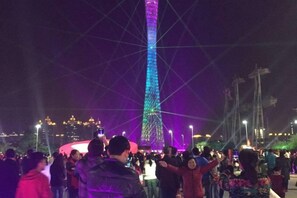 A crowd of people gathered around a tall, illuminated tower structure. - Meicheng Hotel (Guangzhou Zhujiang New Town Subway Station) (Guangzhou)