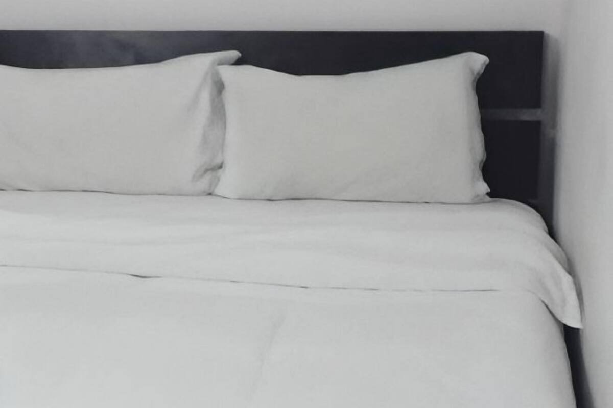 A bed with white bedding and pillows, a dark headboard, and a plain wall.