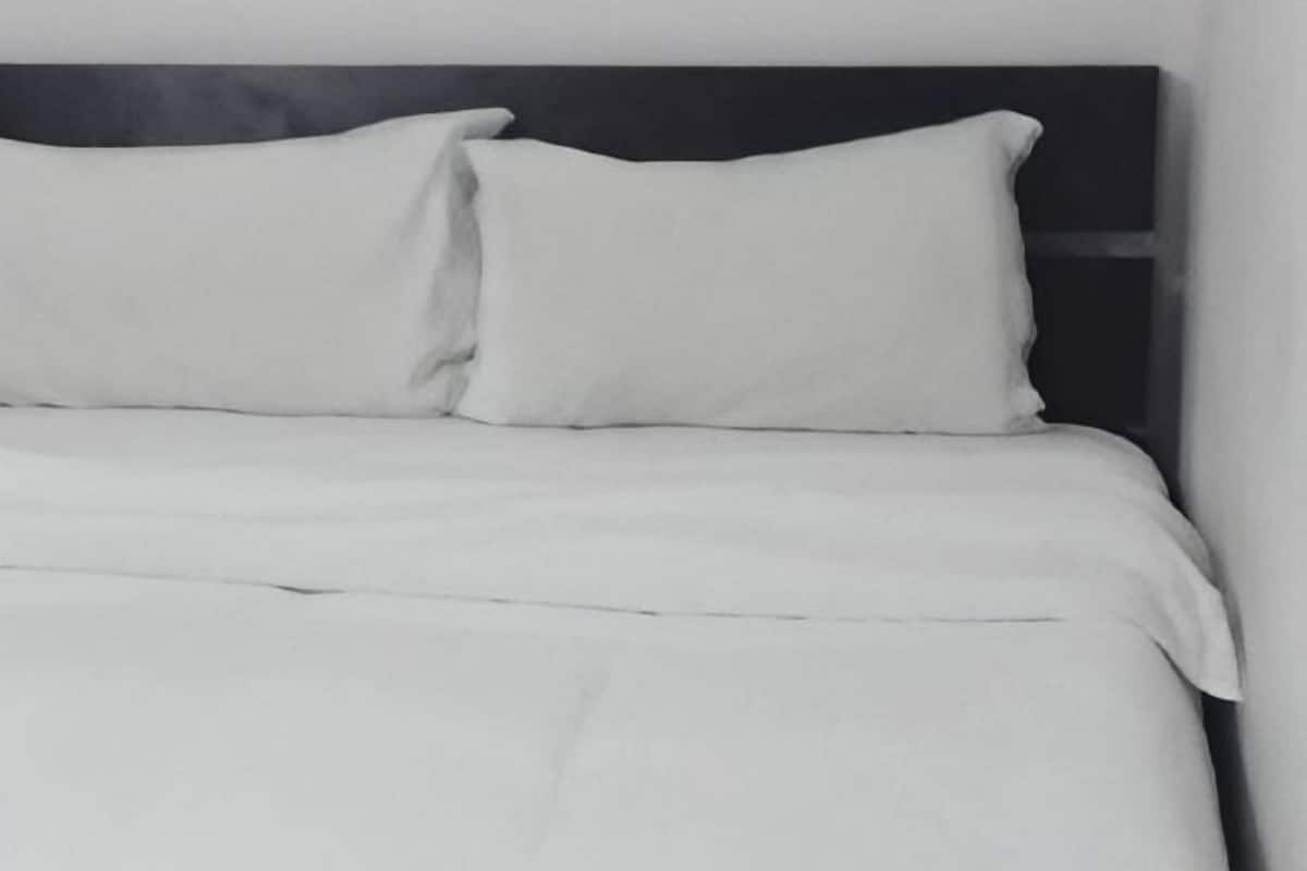 Un lit avec une literie et des oreillers blancs, une tête de lit sombre et un mur sobre.