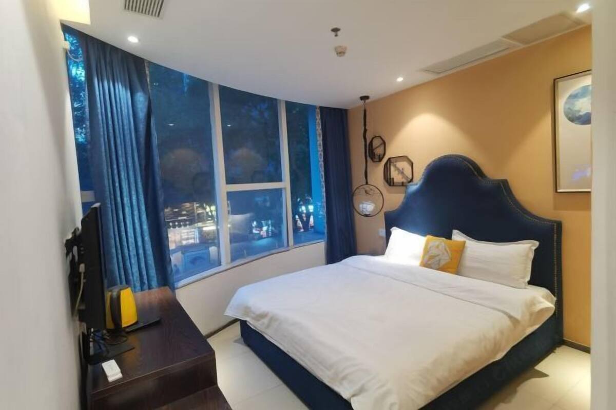 A bedroom with a large bed, a desk with a computer, and a window with curtains.